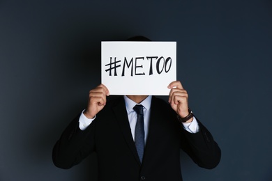 Photo of Man holding paper with text "#METOO" on dark background. Problem of sexual harassment at work