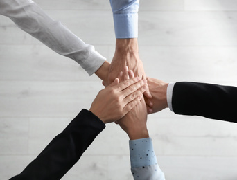 Photo of People holding hands together over light wooden background, top view. Unity concept