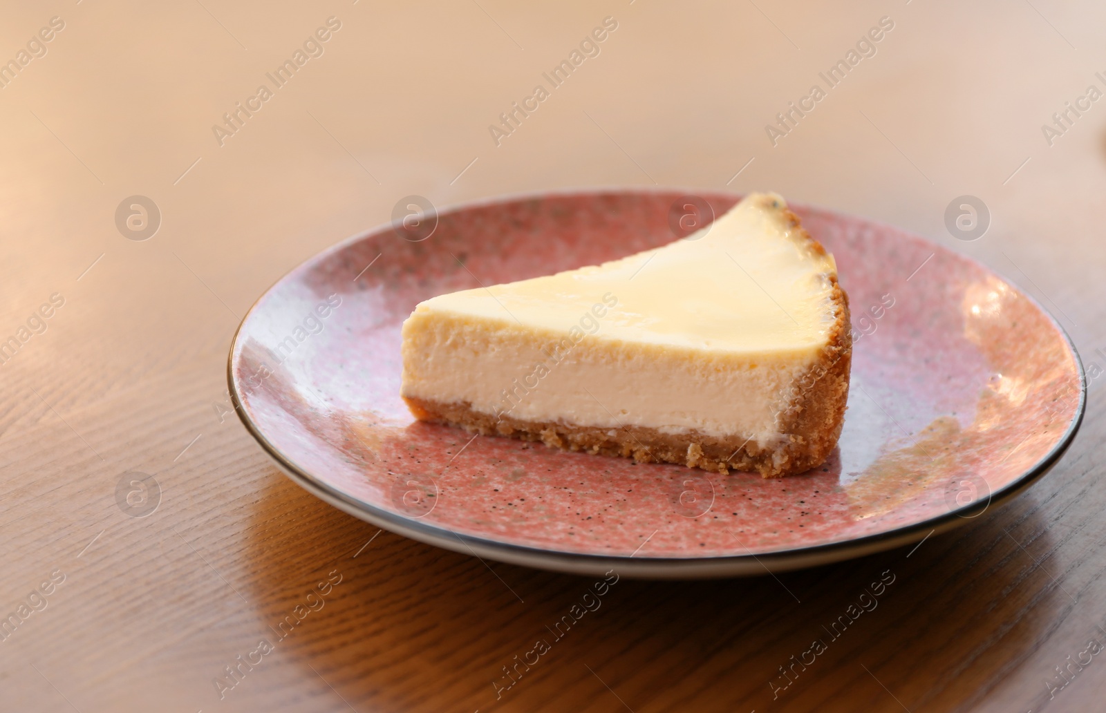 Photo of Plate with slice of cheesecake on wooden table