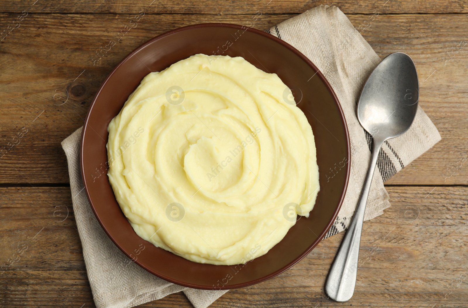 Photo of Freshly cooked homemade mashed potatoes and spoon on wooden table, top view