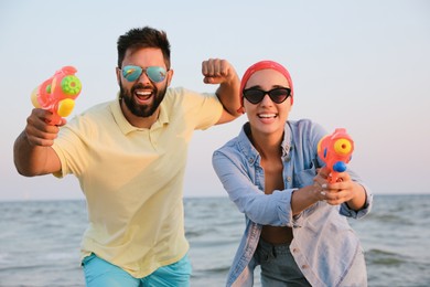 Happy couple with water guns near sea at sunset