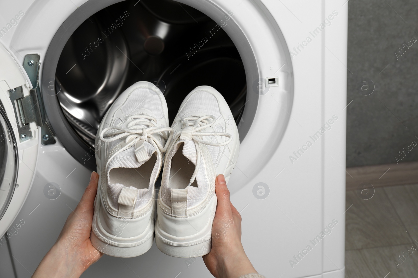 Photo of Woman putting stylish sneakers into washing machine, closeup