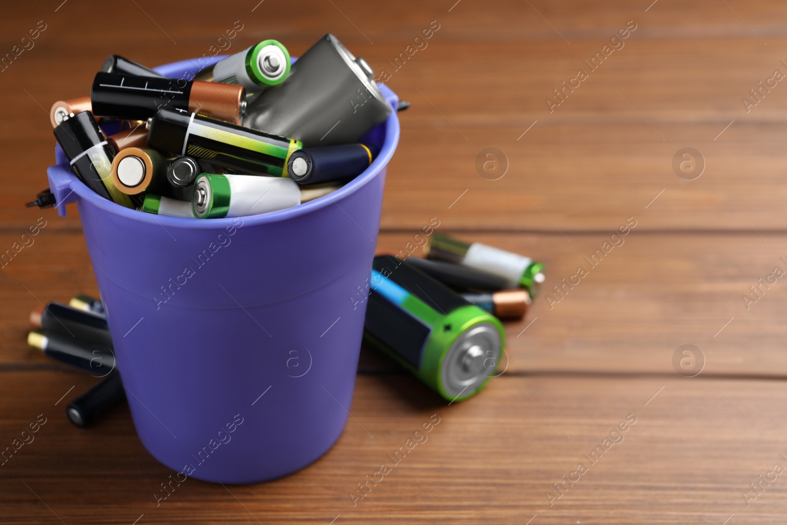 Image of Used batteries and bucket on wooden table, space for text