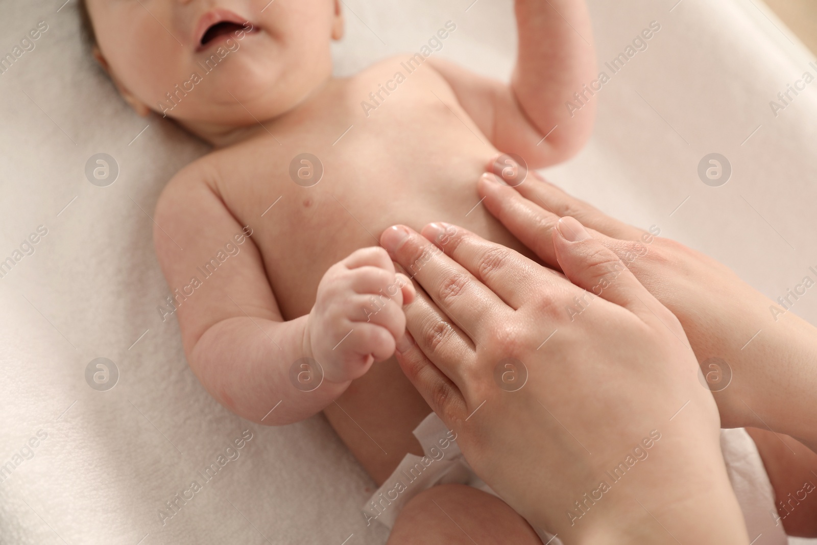 Photo of Mother massaging her baby with oil on changing table, closeup