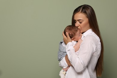 Mother kissing her cute newborn baby on olive background, space for text