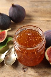Photo of Glass jar with tasty sweet jam, spoons and fresh figs on wooden table, closeup