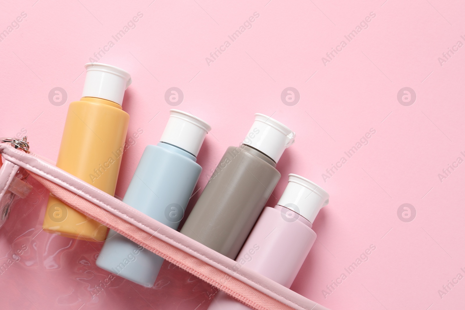 Photo of Plastic bag with cosmetic travel kit on pink background, flat lay. Space for text