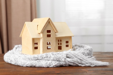 Photo of House model and scarf on wooden table indoors. Heating efficiency