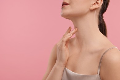 Woman touching her neck on pink background, closeup. Space for text