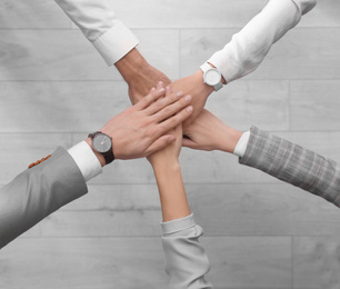 Photo of People holding hands together over light wooden background, top view. Unity concept