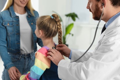 Photo of Mother and daughter having appointment with doctor. Pediatrician examining patient with stethoscope in clinic