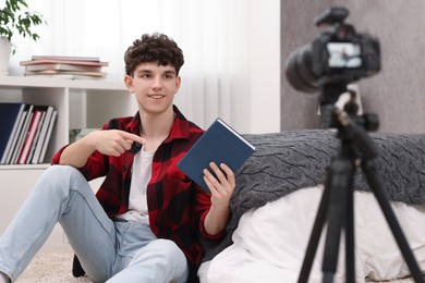 Smiling teenage blogger pointing at book while streaming at home