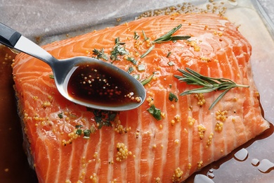 Photo of Spoon with marinade on raw salmon fillet, closeup