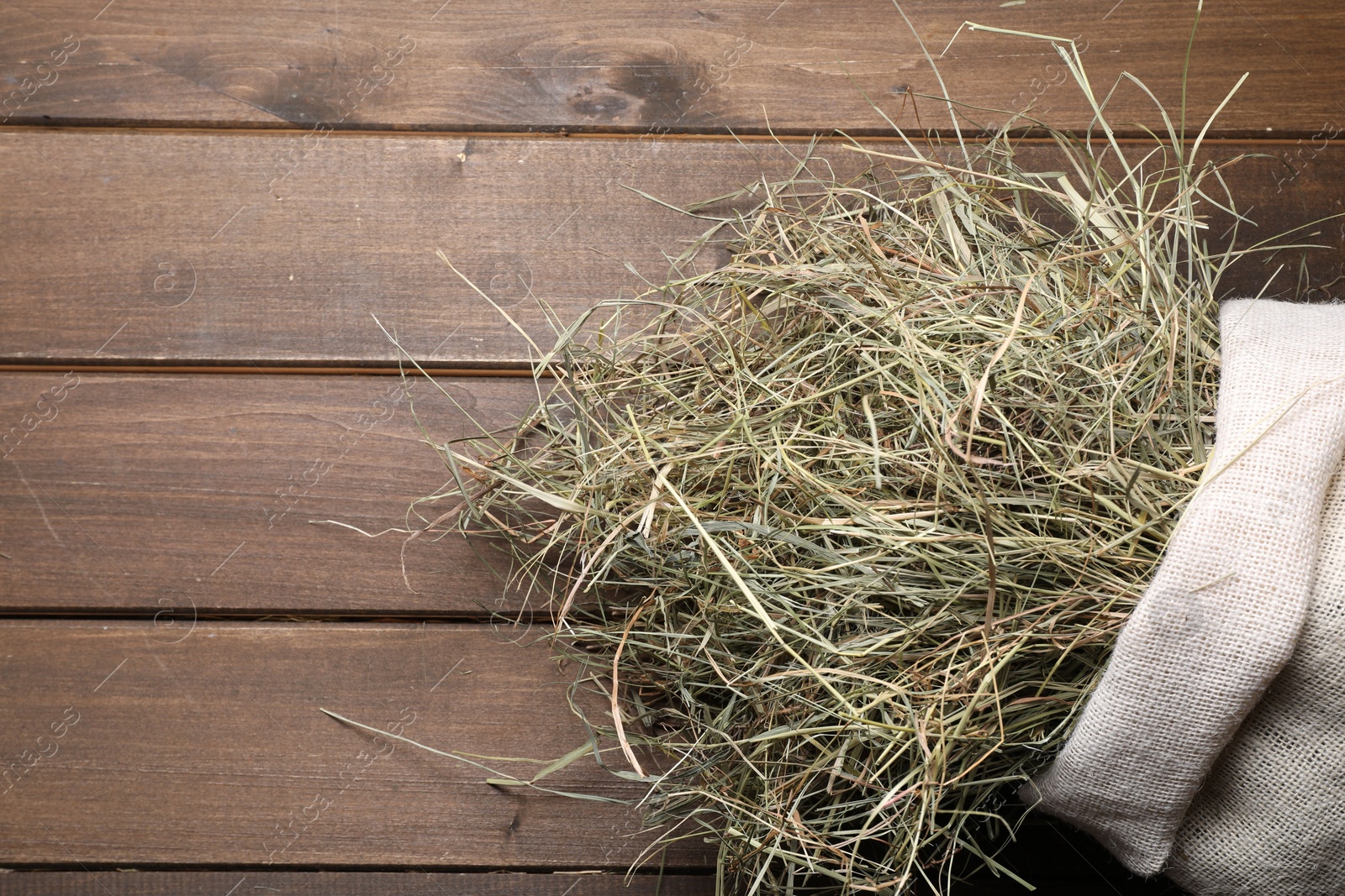 Photo of Dried hay in burlap sack on wooden table, top view. Space for text