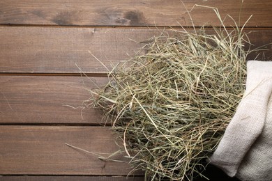 Photo of Dried hay in burlap sack on wooden table, top view. Space for text