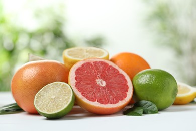 Photo of Different fresh citrus fruits and leaves on white table against blurred background, closeup