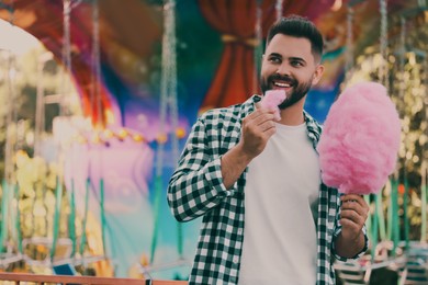 Image of Happy young man eating cotton candy at funfair, space for text