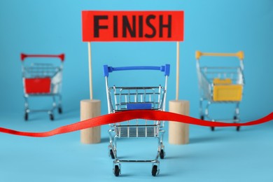 Photo of Shopping cart at red finish line on light blue background. Competition concept
