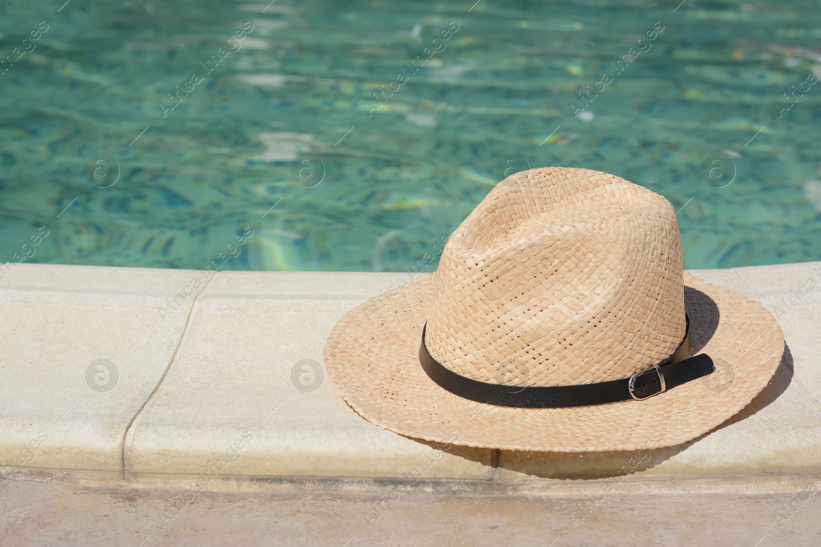 Photo of Stylish hat near outdoor swimming pool on sunny day, space for text. Beach accessory