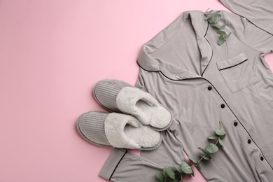 Photo of Pair of slippers, pajamas and eucalyptus branches on pink background, flat lay. Comfortable home outfit