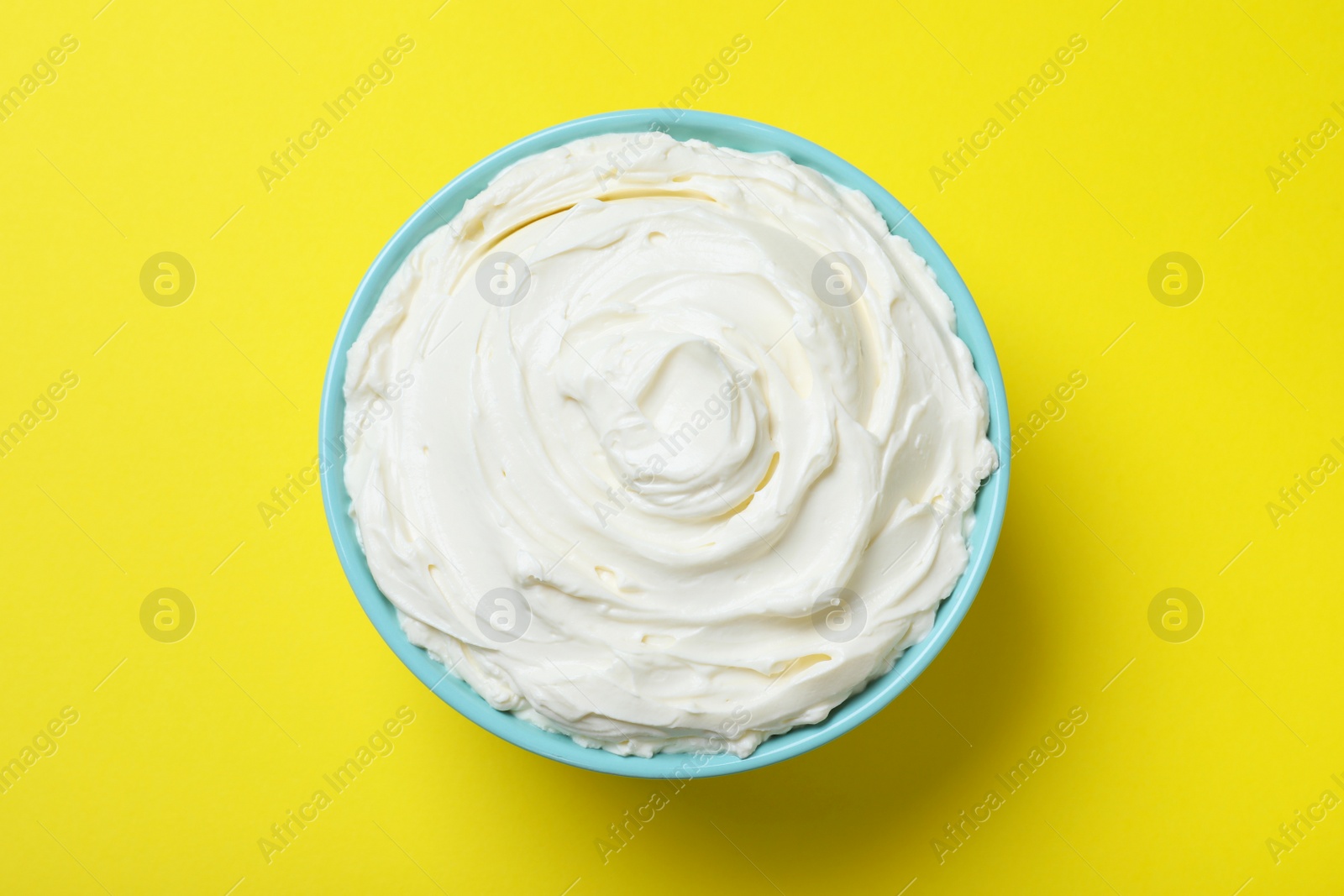 Photo of Bowl of tasty cream cheese on yellow background, top view