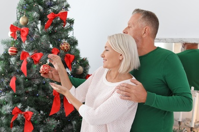 Mature couple decorating Christmas tree together at home