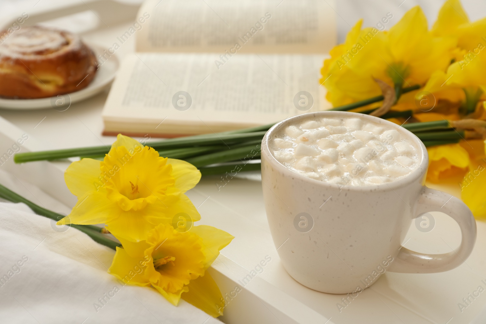 Photo of Beautiful daffodils and cup of hot drink on bed