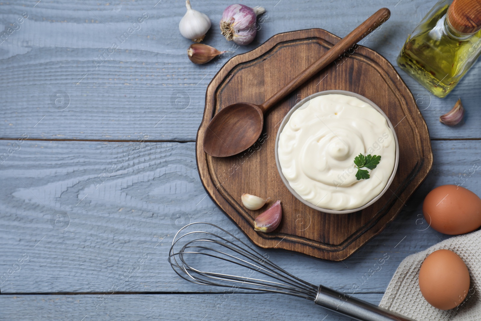 Photo of Tasty mayonnaise in bowl, ingredients and whisk on gray wooden table, flat lay. Space for text