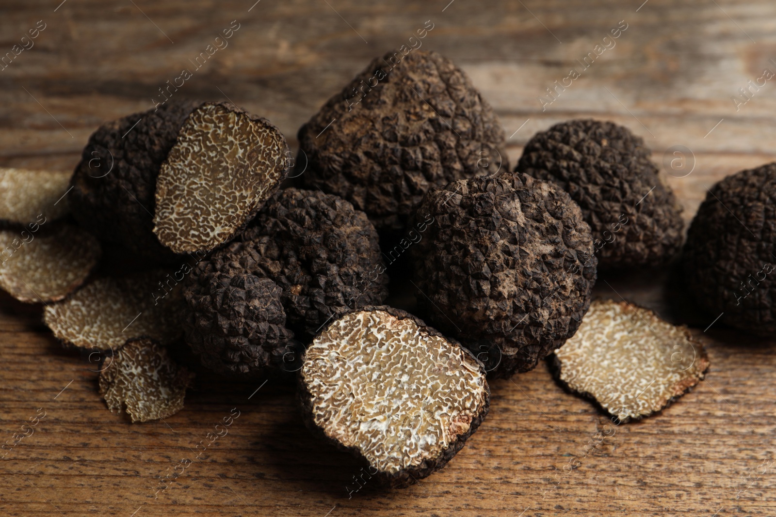 Photo of Whole and cut truffles on wooden table, closeup