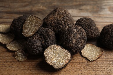 Photo of Whole and cut truffles on wooden table, closeup