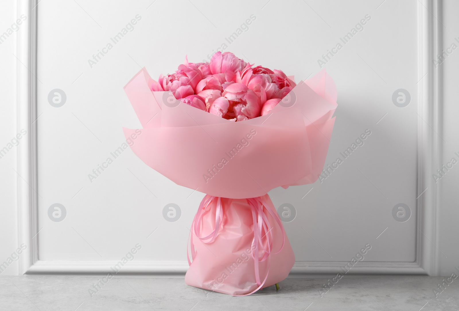 Photo of Bouquet of beautiful pink peonies on table near white wall