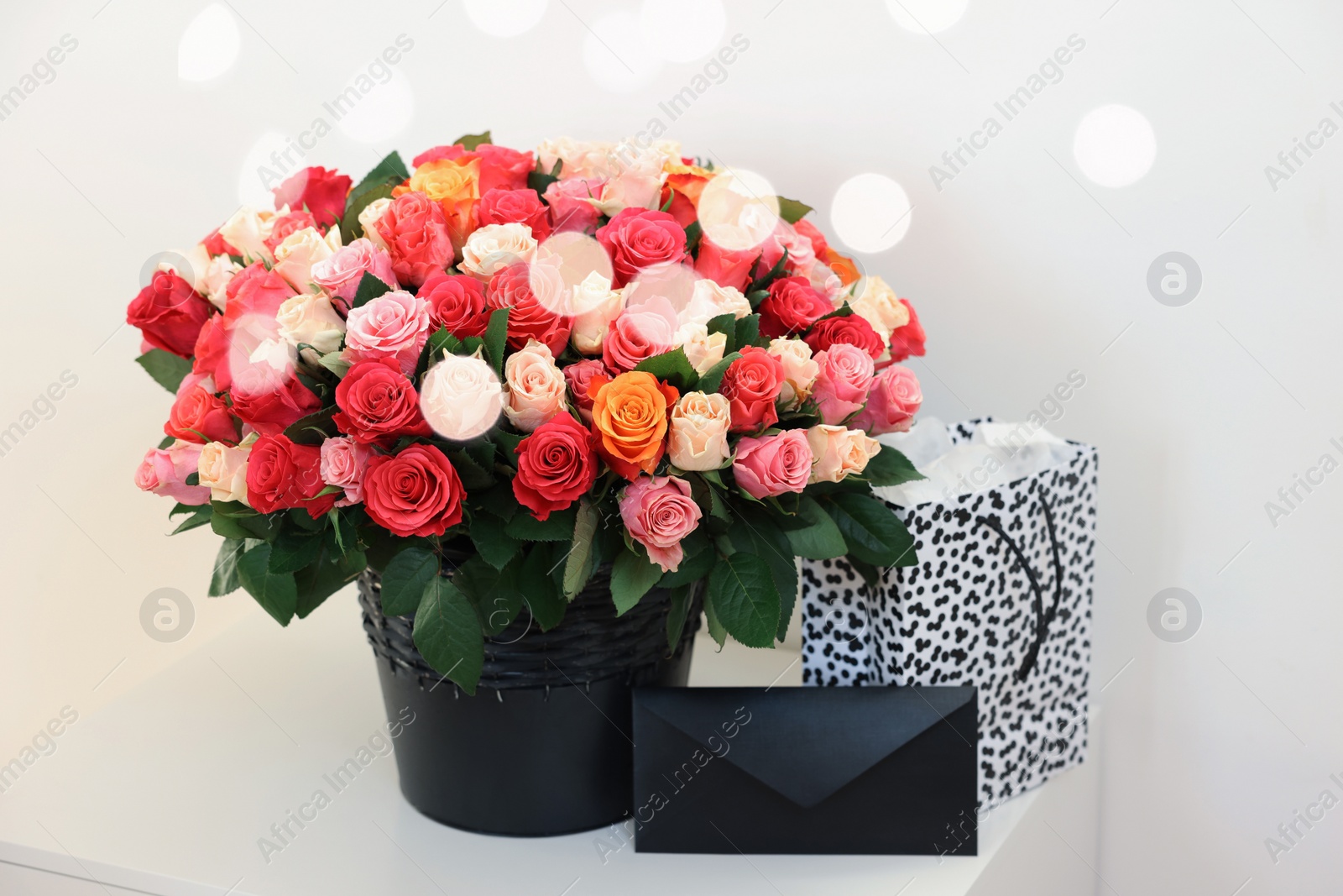 Photo of Bouquet of beautiful roses, envelope and shopping bag on white table