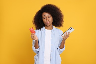 Photo of Confused woman with credit card and smartphone on orange background. Debt problem