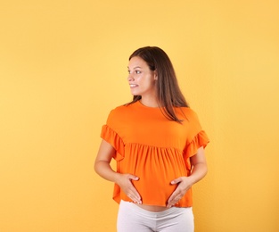 Happy pregnant woman posing on color background