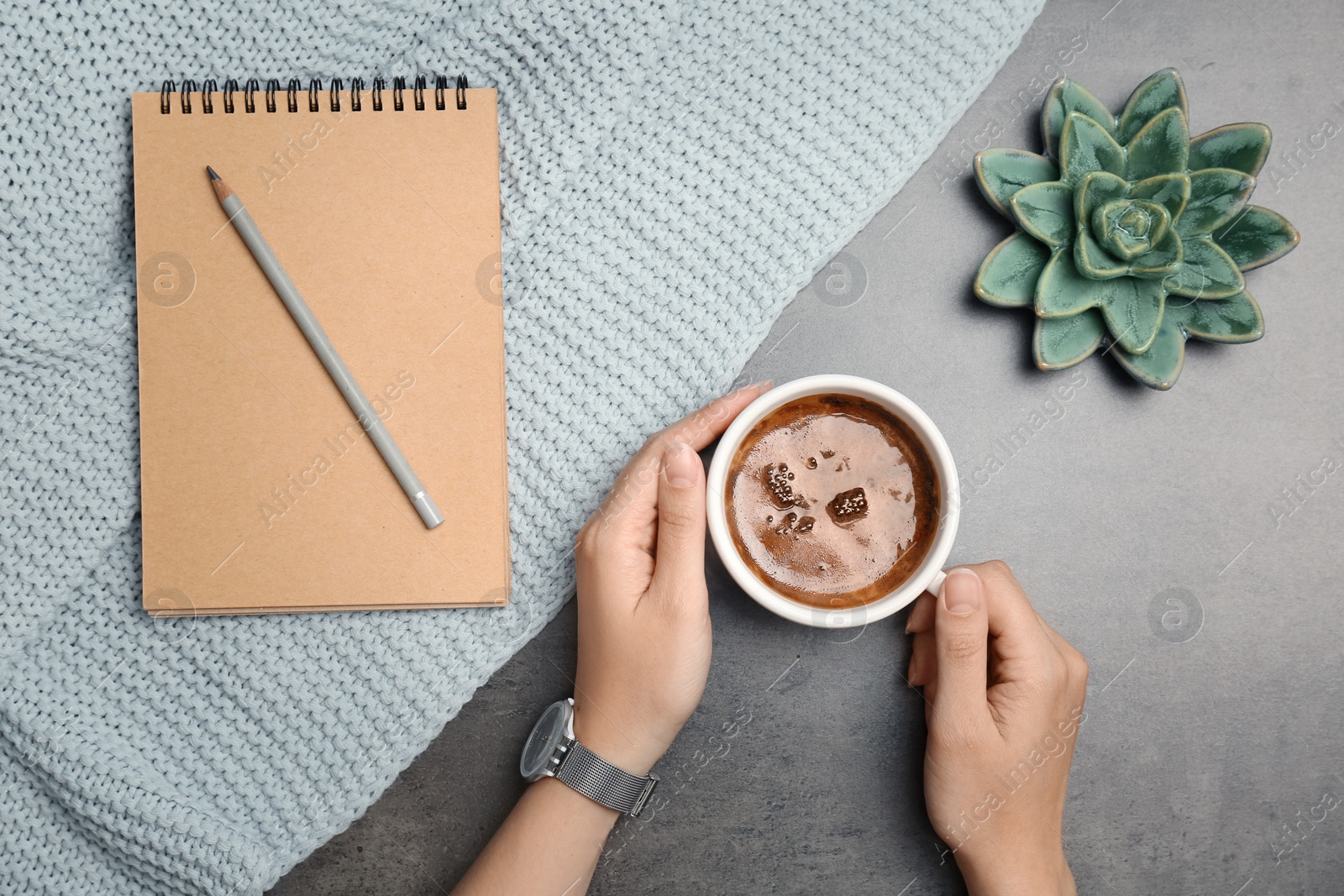 Photo of Young woman with cup of delicious coffee at table, top view