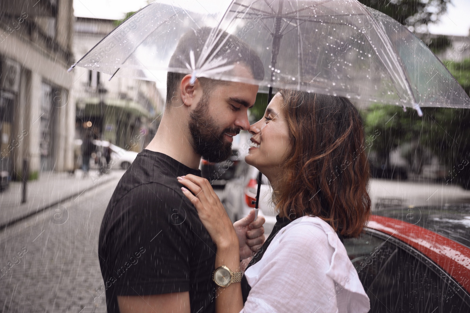 Photo of Young couple with umbrella enjoying time together under rain on city street