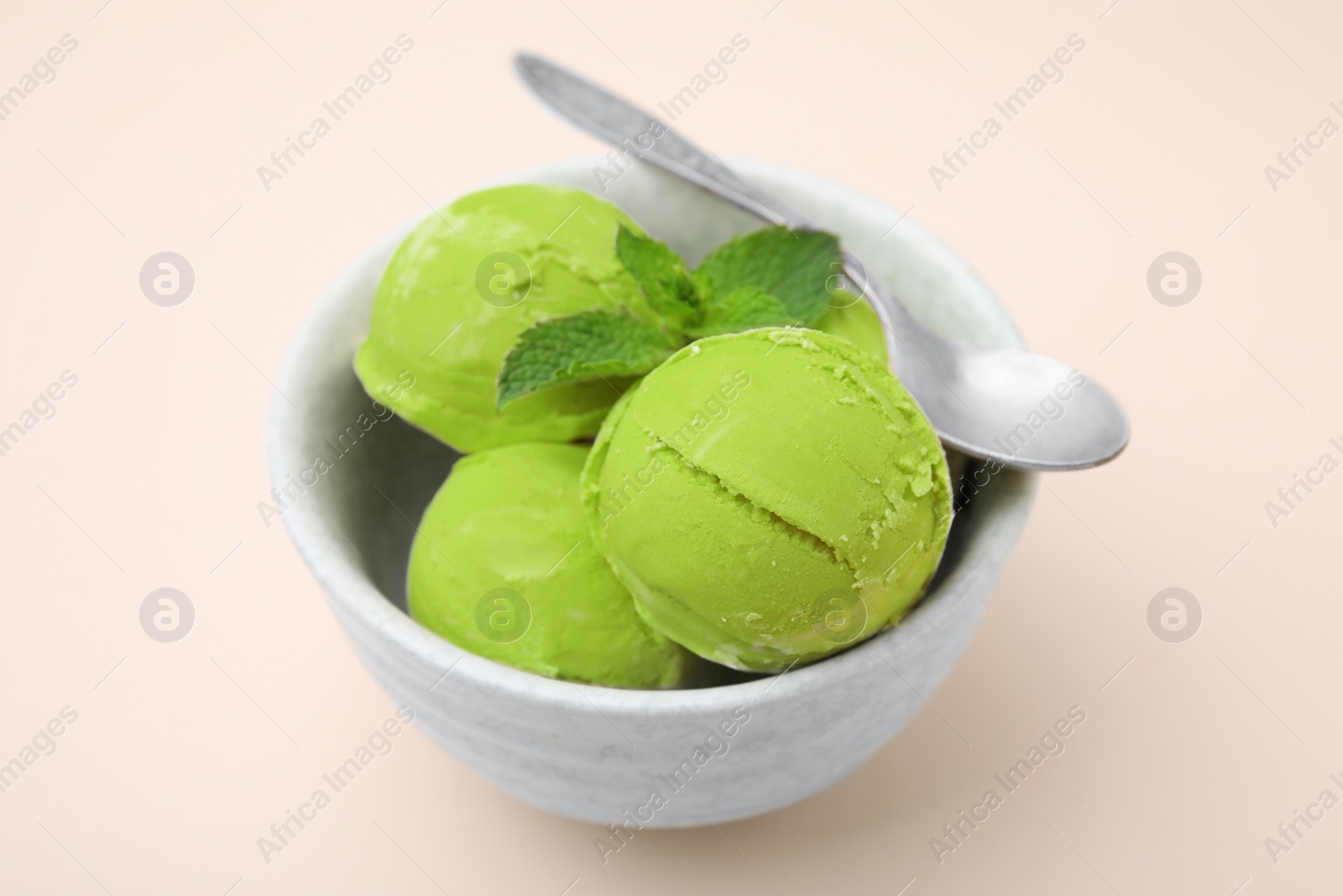 Photo of Tasty matcha ice cream and spoon in bowl on beige table, closeup