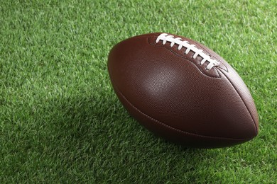 Photo of Leather American football ball on green grass. Space for text