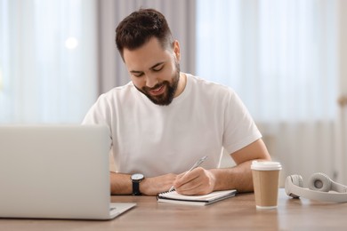 Young man writing down notes during webinar at table in room