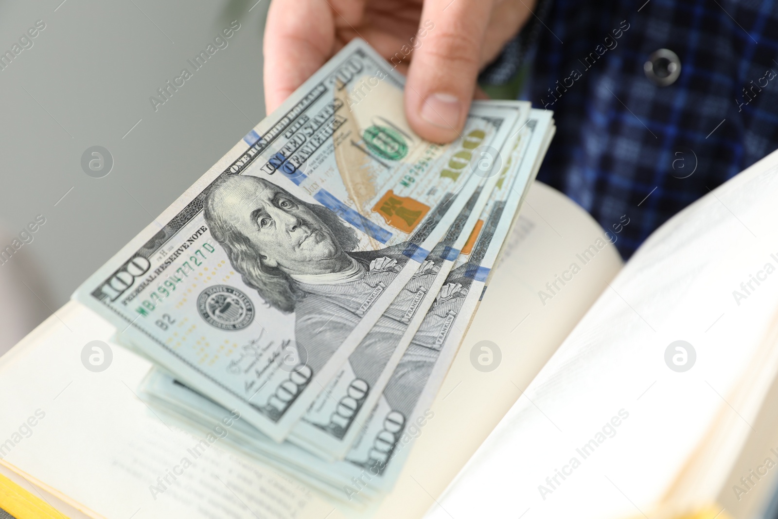 Photo of Man hiding dollar banknotes in book indoors, closeup. Money savings