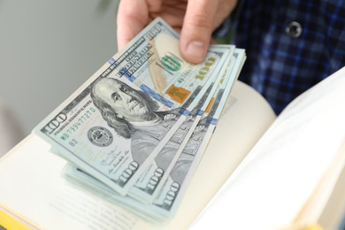 Photo of Man hiding dollar banknotes in book indoors, closeup. Money savings