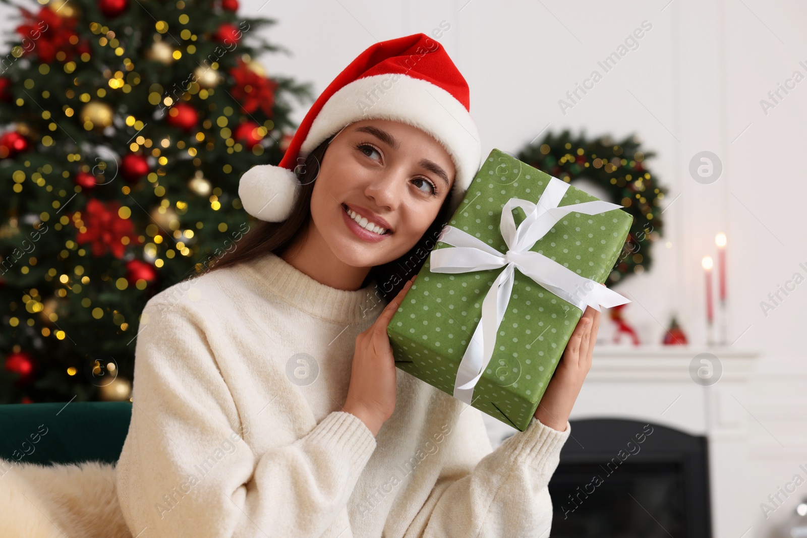 Photo of Happy young woman in Santa hat with Christmas gift at home