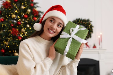 Happy young woman in Santa hat with Christmas gift at home