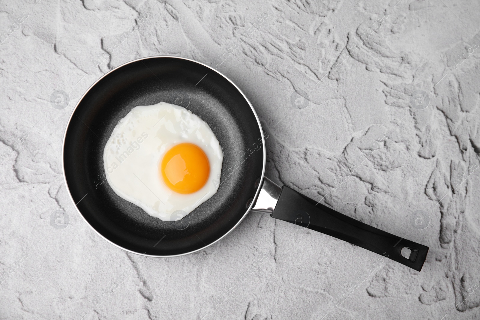Photo of Tasty fried egg in pan on white textured table, top view