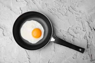 Tasty fried egg in pan on white textured table, top view