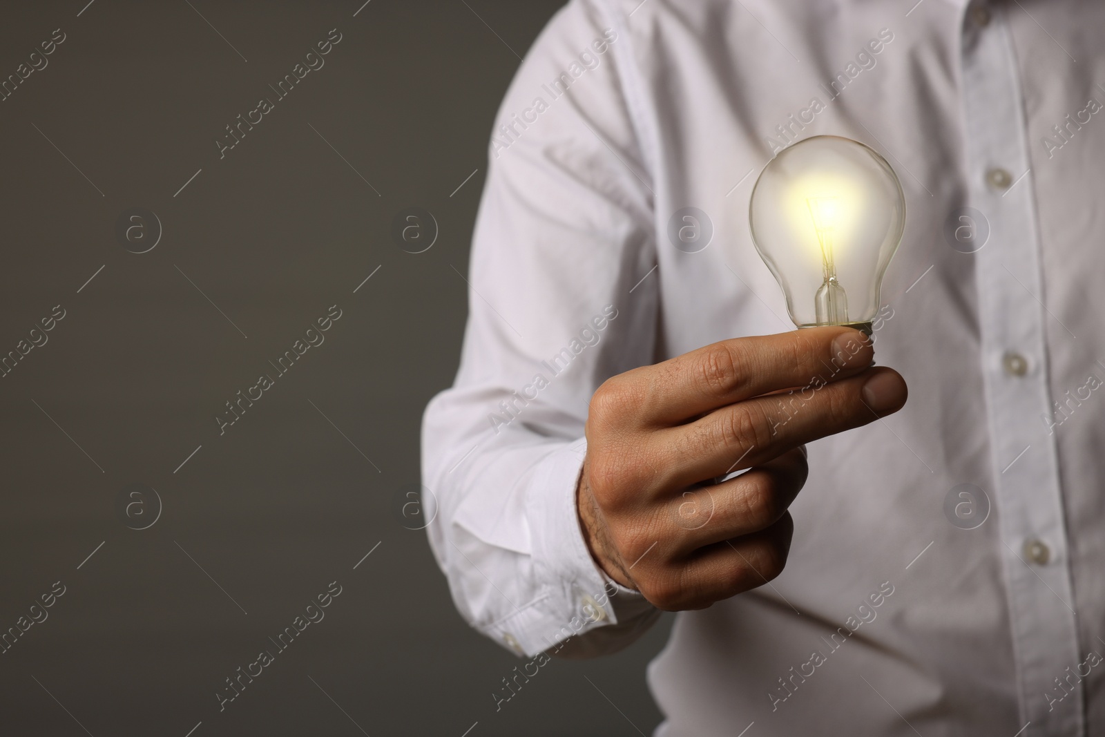 Photo of Glow up your ideas. Closeup view of man holding light bulb on grey background, space for text