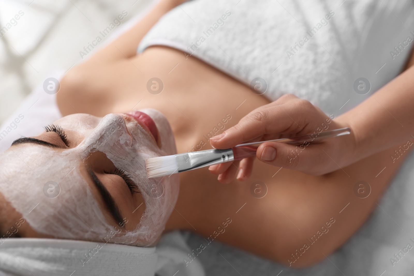 Photo of Cosmetologist applying mask on woman's face in spa salon, closeup