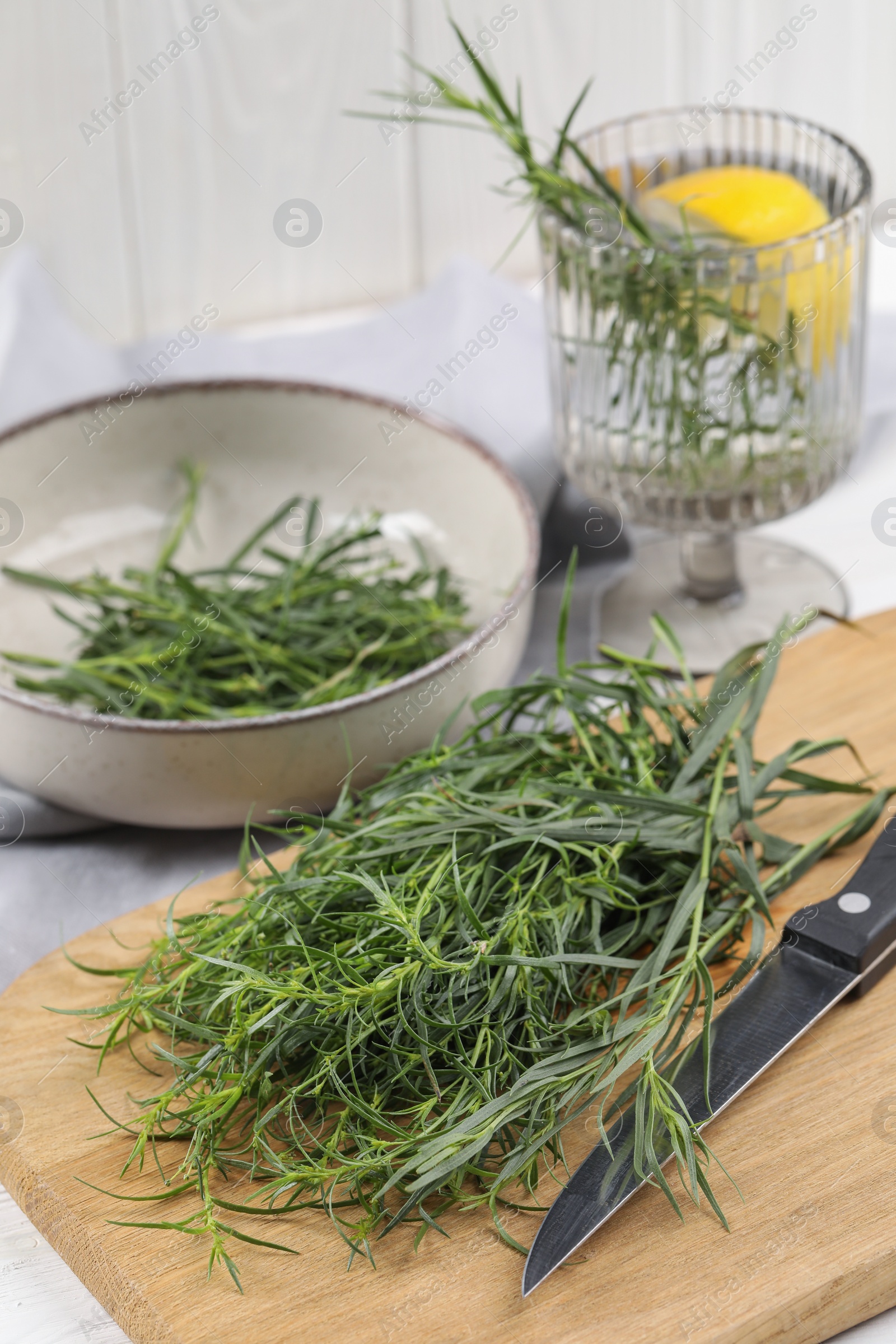 Photo of Fresh tarragon sprigs and knife on wooden board, closeup