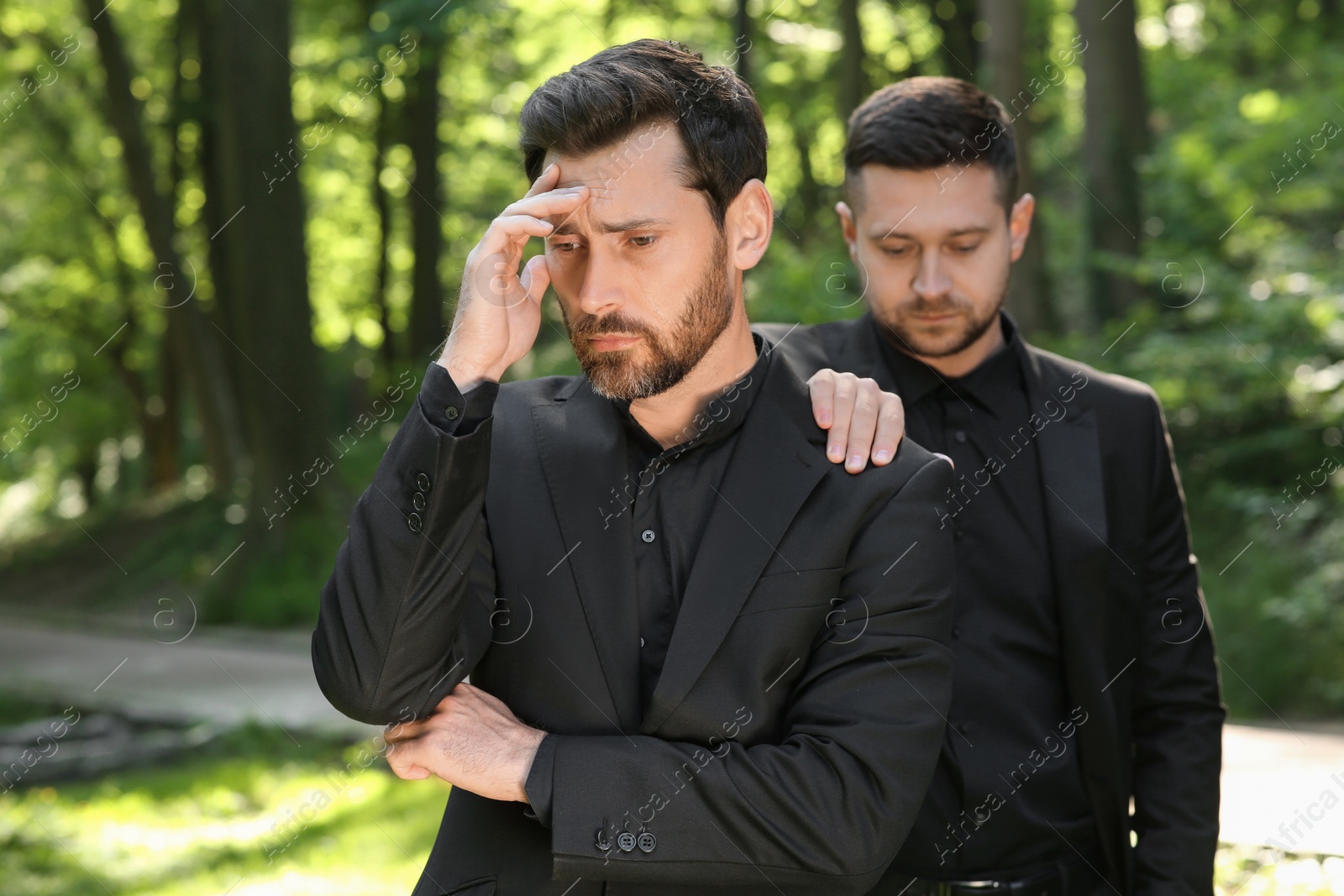 Photo of Funeral ceremony. Man comforting his friend outdoors