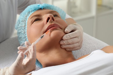 Doctor giving lips injection to senior woman in clinic, closeup. Cosmetic surgery